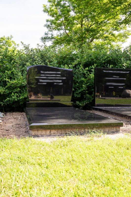 Klassiek grafmonument van zwart gepolijst graniet met golvend kopstuk en dekplaat