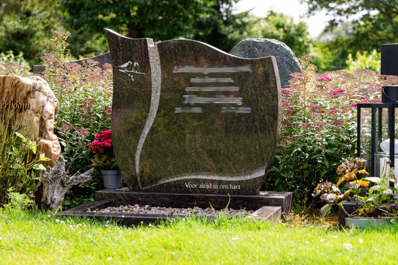 Golvend grafmonument van bruin-groen graniet met de tekst 'Voor altijd in ons hart'