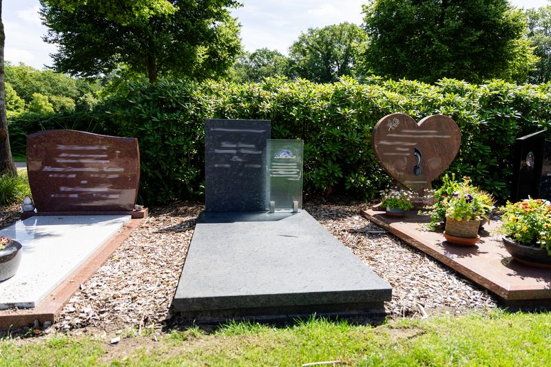 Grafmonument van donker graniet met glazen gedenkpaneel, geplaatst tussen het groen