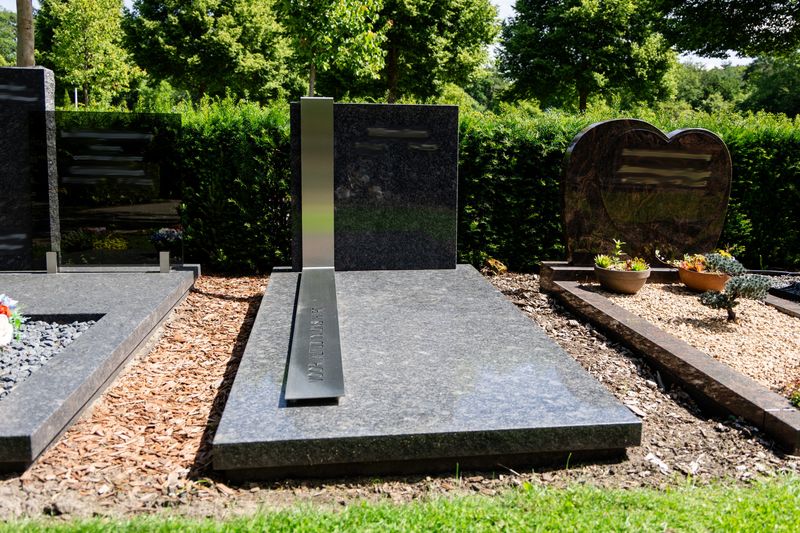 Eigentijds grafmonument van donker graniet met een RVS-band over de dekplaat